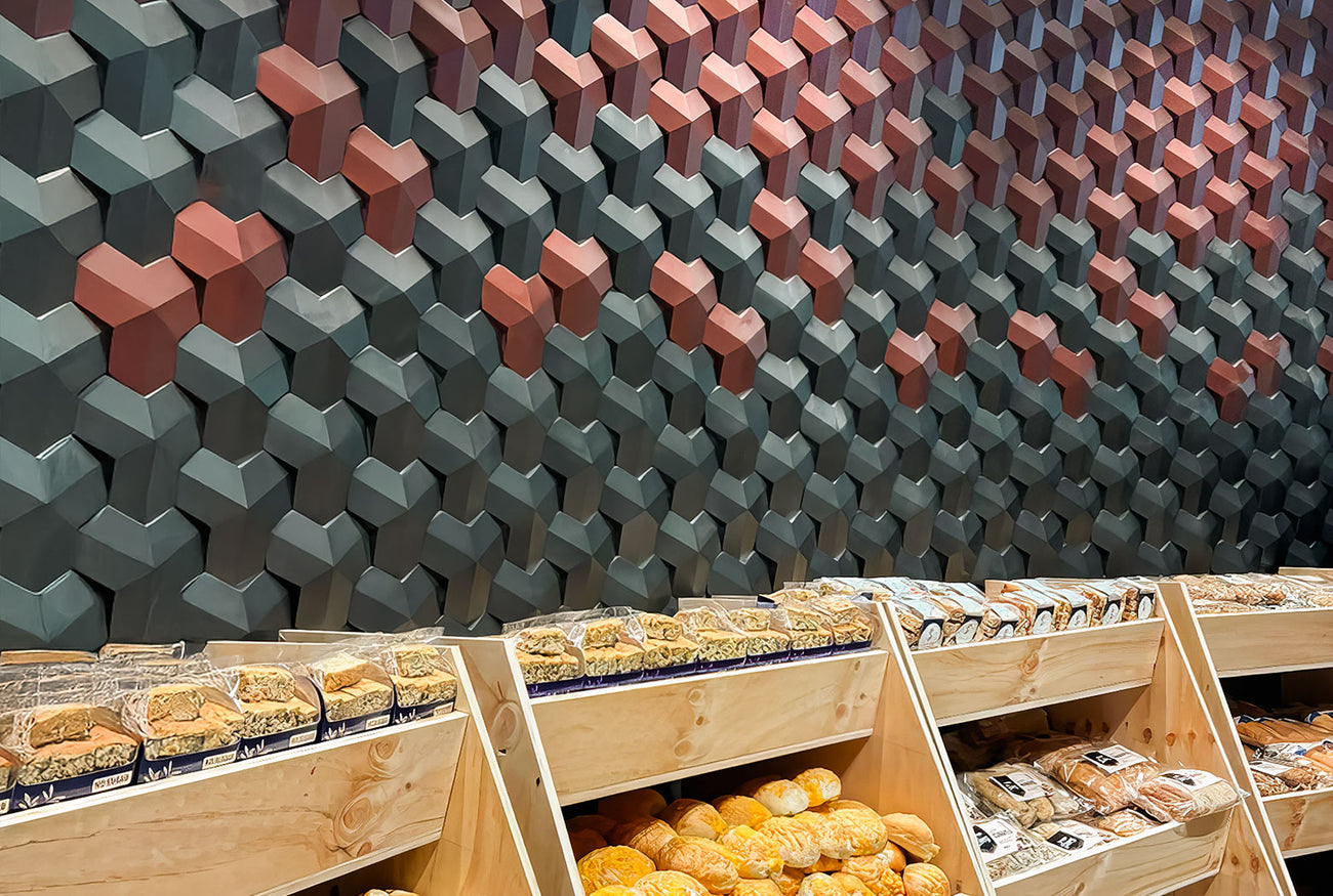 Modern bakery with geometric 3D concrete wall tiles in green and terracotta tones, creating a stylish and contemporary retail interior design.