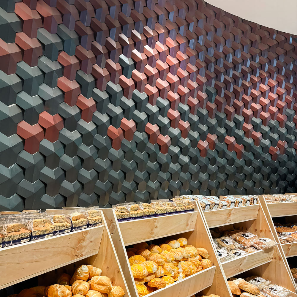 Bakery interior with a striking 3D wall tile design in shades of green and red, creating a textured geometric pattern behind wooden shelves filled with fresh bread and pastries.