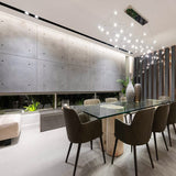 Elegant dining room featuring a modern glass table, upholstered chairs, and a striking feature wall made of concrete panels, enhanced by unique pendant lighting and natural decor elements