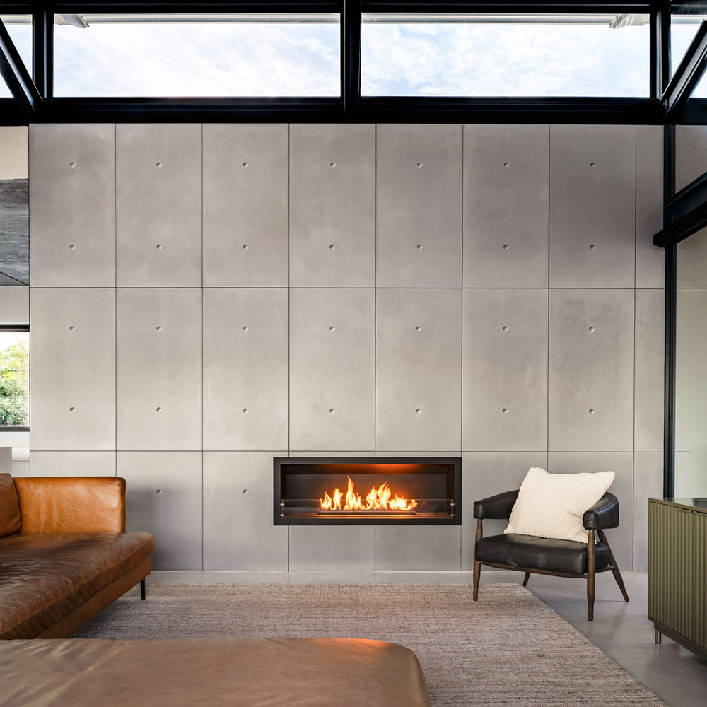Modern living room with fireplace and floor-to-ceiling concrete panel interior wall, leather seating, and large windows.