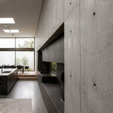 Modern minimalist kitchen interior featuring dark wood cabinetry, concrete wall paneling with visible screw holes, a black countertop with integrated sink, and a large window looking out onto greenery. - FLOAT concrete