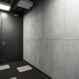 Commercial interior with lightweight grey concrete wall panels and black door, featuring acoustic ceiling elements and dark carpet flooring with light square inlays.